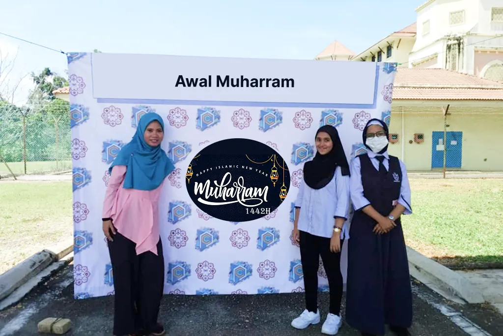Teachers and a student standing in front of an Awal Muharram celebration banner.