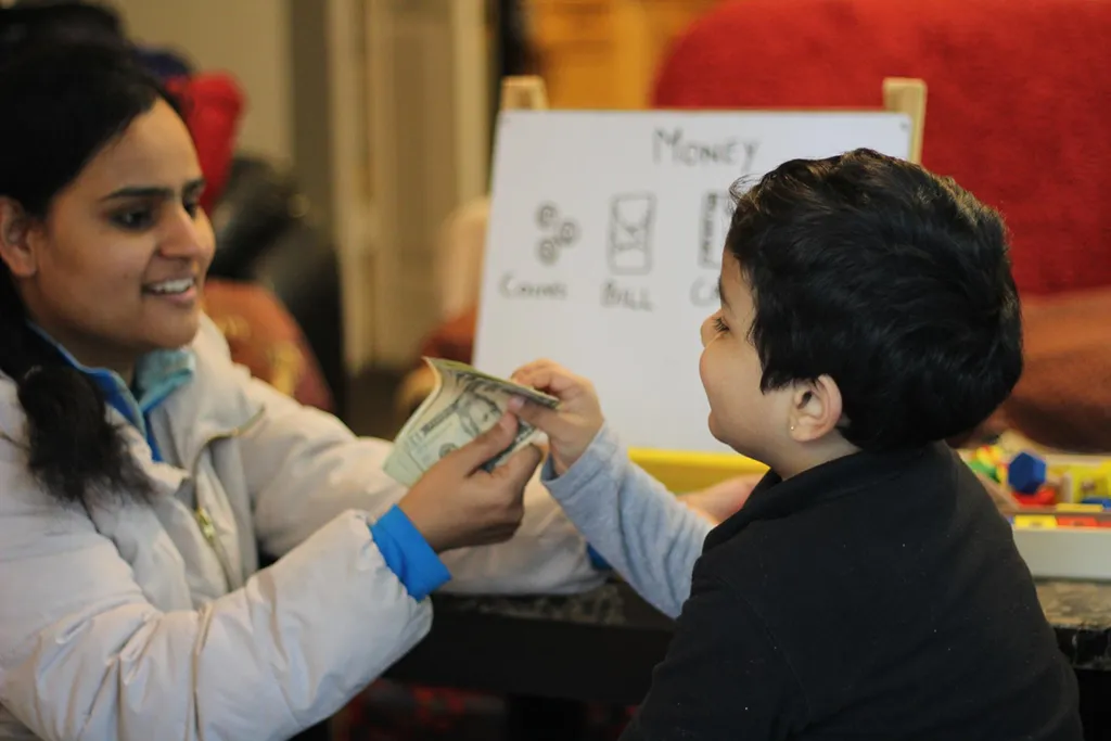 Teacher gives a young student a hands-on financial literacy lesson, using a cash bill to explain money management.